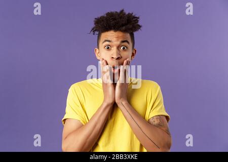 Ritratto di astuto, intrigato giovane hispaic hipster ragazzo ascoltare impressionante storia interessante, tenere le mani sul viso divertito, pettegolezzi, stare Foto Stock