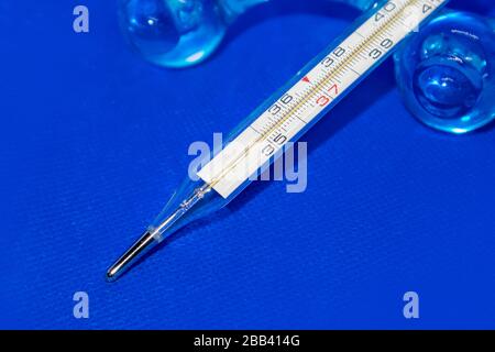 Termometro macro, strumento a mercurio, misurazione, indicazione della temperatura strumento medico su sfondo blu vibrante Foto Stock
