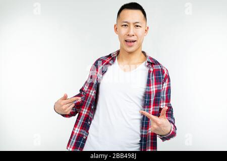 Sorridente giovane asiatico in una camicia a scacchi ampio spazio aperto mostra spazio vuoto sulla sua T-shirt bianca su un isolato sfondo bianco studio. Foto Stock