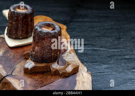 Cannelés (Canelés) de Bordeaux la ricetta è una piccola pasta con rum e vaniglia su un piatto di legno. Dolce tradizionale francese con gustosi spuntini. Obliquo Foto Stock