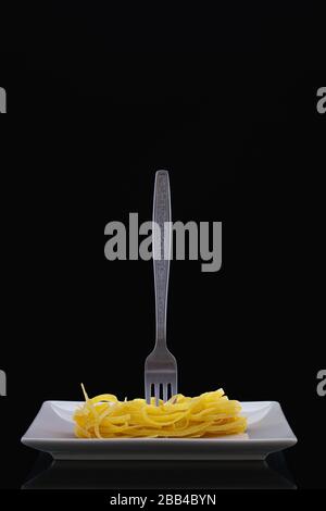 Forchetta e tagliatelle in acciaio inox sul piatto bianco nella stanza buia. Pranzo dietetico. Foto Stock