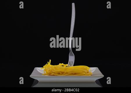 Forchetta e tagliatelle in acciaio inox sul piatto bianco nella stanza buia. Pranzo dietetico. Foto Stock