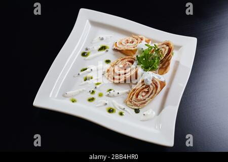 Vista dall'alto di quattro panini a fette con pasta e salmone serviti con rucola per insalata, pesto e panna acida su piatto bianco. Piatto saporito isolato su un tavolo di legno nero nel ristorante. Concetto di cucina. Foto Stock