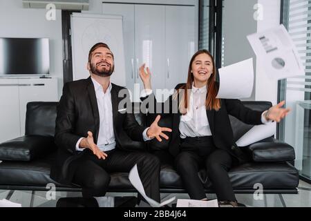 All'ufficio moderno, due di uomini d'affari e businesswoman sono fogli di carta trotwing nell'aria dopo il lavoro finito e riuscito sul loro obiettivo Foto Stock