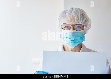 Il medico con maschera facciale in ospedale tiene un segnale di avvertimento bianco durante l'epidemia di coronavirus di Covid-19 Foto Stock