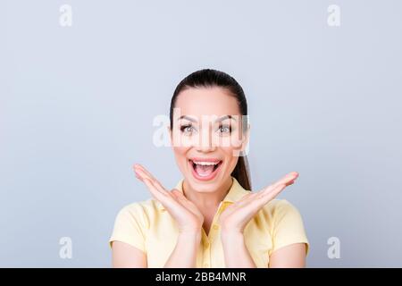 Nessun modo! Davvero?! Scioccata giovane ragazza attraente sta tenendo le sue palme vicino al suo viso. Lei è eccitata e con la bocca aperta su puro sfondo di luce, è Foto Stock