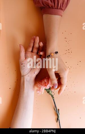 Mani femminili con braccialetti pendenti e fiore rosa uno sfondo arancione luminoso con luccichio Foto Stock