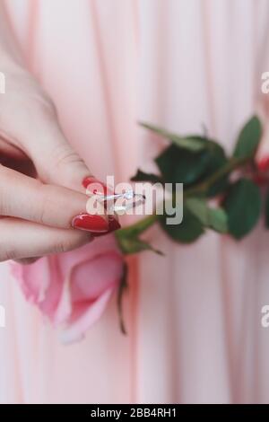 Primo piano verticale di una femmina che tiene un diamante d'argento anello e una rosa Foto Stock