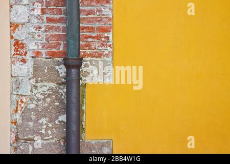 Vecchio rame arrugginito e tubo discendente in ghisa contro un muro di mattoni e intonaco. Foto Stock