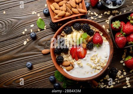 Appartamento laici vista superiore a frutto sano muesli con banana fragola mandorle e blackberry con yogurt in argilla piatto di legno sul tavolo da cucina Foto Stock