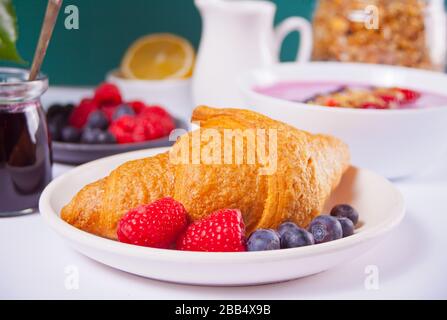 Croissant freschi panini, bacche, marmellata di ribes nero e ciotola di frullato. Concetto di colazione Foto Stock