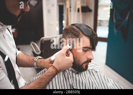 Il parrucchiere è attentamente focalizzato sul taglio dei capelli del cliente. Foto Stock