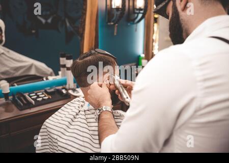 Parrucchiere realizza una macchina per il taglio dei capelli per il cliente. Ragazzo taglio capelli in barbiere Foto Stock