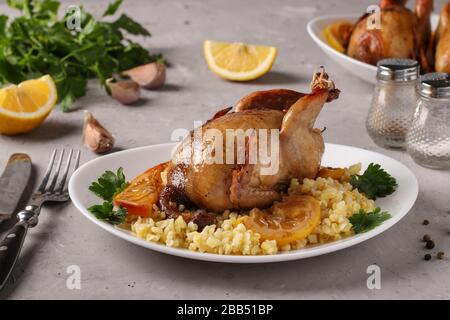 Quaglie al forno con limone e arancio servite con bulgur su un piatto bianco su uno sfondo grigio Foto Stock