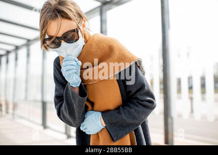 Donna in maschera viso sentirsi male, tosse a una fermata dei trasporti pubblici all'aperto. Concetto di epidemia di Coronavirus Foto Stock