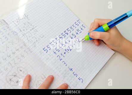 Le mani del capretto che fanno i compiti di matematica. Primo piano di giovane ragazzo mano tenendo la penna e scrivere un lavoro di matematica primo piano. Concetto di istruzione a hom Foto Stock