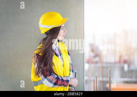 Operaio di costruzione ragazza pensiva. Giovane ingegnere femminile che guarda un cantiere Foto Stock