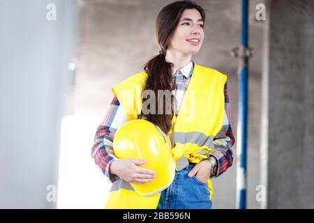 Ingegnere femminile si trova in un cantiere e tiene un cappello in mano Foto Stock