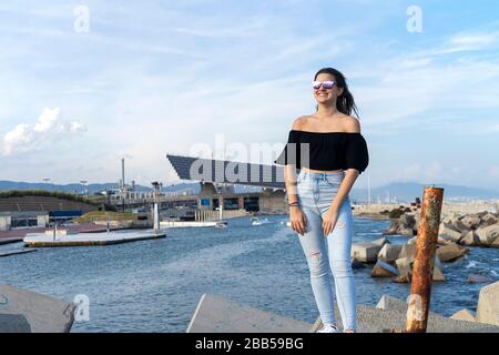 Una giovane bella donna felice con i capelli lunghi in piedi sul lungomare mentre guardando la macchina fotografica Foto Stock