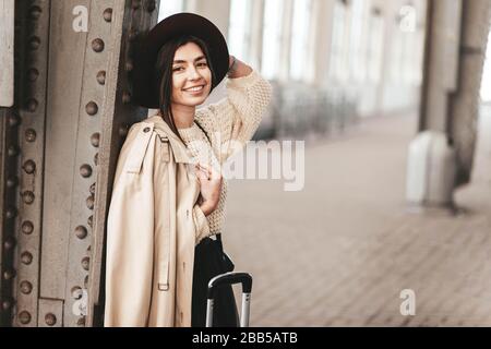 Ritratto di giovane donna bella viaggiatore in casual cappotto e cappello che è in attesa di un treno sulla piattaforma della stazione ferroviaria Foto Stock