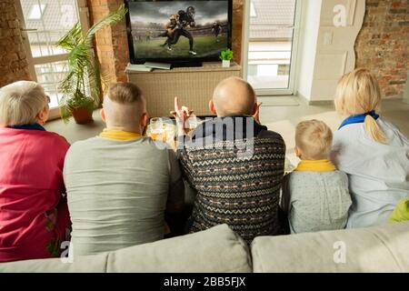 La famiglia caucasica entusiasta che guarda il campionato americano di calcio, partita di sport a casa. Nonni, genitori e ragazzino che si rallegrano per la squadra nazionale preferita. Concetto di emozioni, sostegno, insieme. Foto Stock