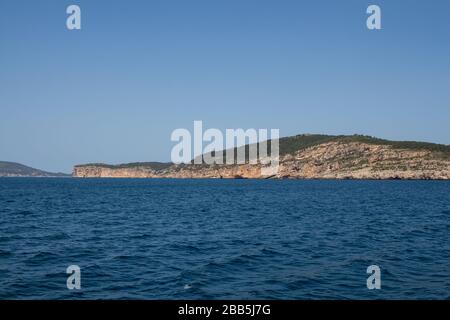 Vista da una barca sulle acque blu profondo del Mediterraneo e costa rocciosa all'orizzonte. Parco Naturale Regionale di Porto Conte, w Foto Stock