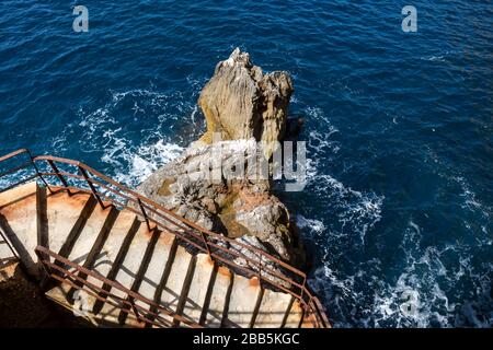 Vecchie scale in cemento che fiancheggiano una scogliera con un corrimano arrugginito. Roccia nel mare Mediterraneo accanto. Grotta di Nettuno, isola Sardegna, Italia. Foto Stock