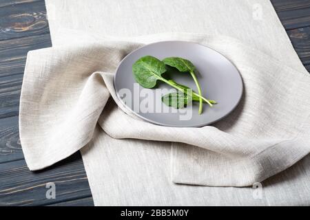 Spinaci freschi foglie su un piatto grigio su una tovaglia di lino Foto Stock