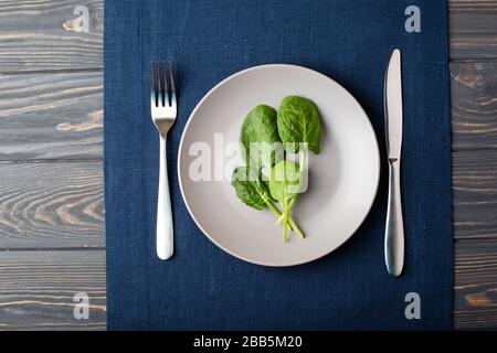 Foglie di spinaci freschi su un piatto grigio su tovaglia di lino blu Foto Stock