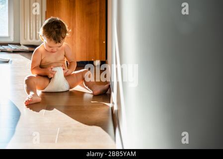 La ragazza del bambino al mattino si sveglia e controlla il suo pannolino bagnato curiosamente. Foto Stock