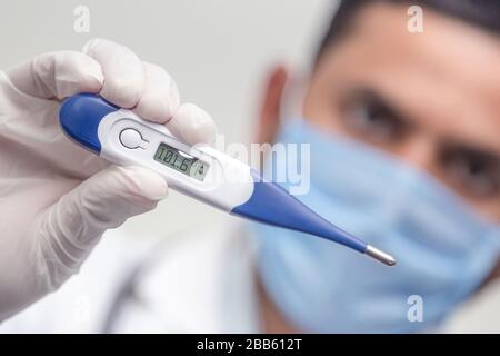 Il medico che indossa lo stetoscopio tiene il termometro medico digitale per misurare la temperatura corporea, la protezione da virus, influenza e malattie respiratorie. Coron Foto Stock