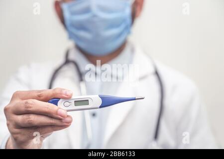 Il medico che indossa lo stetoscopio tiene il termometro medico digitale per misurare la temperatura corporea, la protezione da virus, influenza e malattie respiratorie. Coron Foto Stock