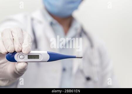 Il medico che indossa lo stetoscopio tiene il termometro medico digitale per misurare la temperatura corporea, la protezione da virus, influenza e malattie respiratorie. Coron Foto Stock