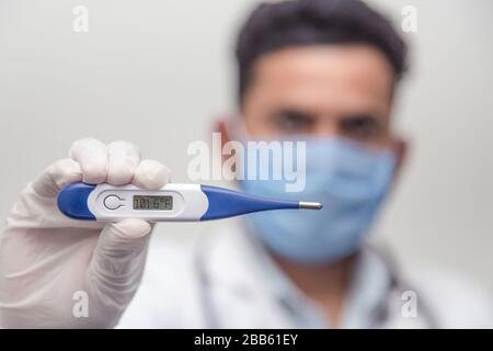 Il medico che indossa lo stetoscopio tiene il termometro medico digitale per misurare la temperatura corporea, la protezione da virus, influenza e malattie respiratorie. Coron Foto Stock
