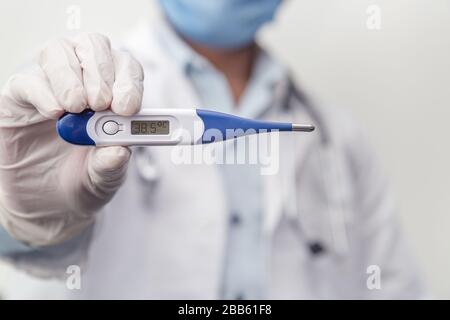 Il medico che indossa lo stetoscopio tiene il termometro medico digitale per misurare la temperatura corporea, la protezione da virus, influenza e malattie respiratorie. Coron Foto Stock