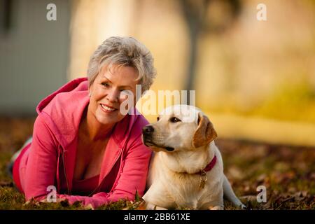 Donna attiva senior sdraiata in un parco con il suo cane Foto Stock