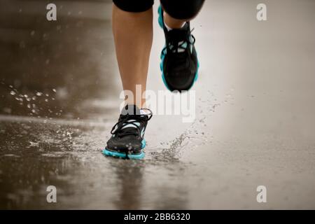 Young woman jogging on a residential street in the rain. Foto Stock