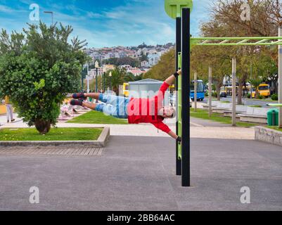 Un giovane uomo in forma mostra la sua forza con una bandiera umana tenere sulle barre di muro in piedi libera in un parco pubblico a Funchal, Madeira in una giornata di sole. Foto Stock