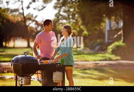 Coppia sorridente cottura su un barbecue nel loro back yard. Foto Stock