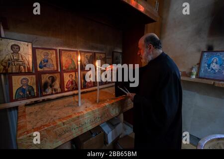 (200330) -- BETLEMME, 30 marzo 2020 (Xinhua) -- UN sacerdote accende una candela durante una Messa domenicale in una chiesa ortodossa a Beit Sahour, vicino alla città di Betlemme della Cisgiordania, il 29 marzo 2020. Per la prima volta in assoluto, Raed al-Atrash, un uomo palestinese di 54 anni della città di Betlemme, ha partecipato alla Messa domenicale con la sua famiglia attraverso una trasmissione televisiva dal vivo, poiché le chiese sono chiuse come parte delle precauzioni contro la diffusione del romanzo coronavirus.TO ANDARE CON 'Feature: I cristiani in Palestina frequentano le preghiere dal vivo mentre le chiese si chiudono sulle paure del coronavirus (Foto di Luay Sababa/Xi Foto Stock