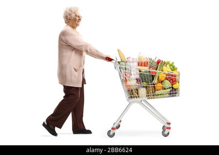 Profilo a tutta lunghezza di una donna anziana che spinge un carrello pieno di cibo isolato su sfondo bianco Foto Stock