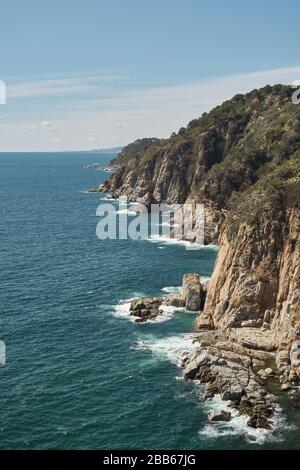 Buchi che si rompono sulle rocce delle scogliere sul mare Mediterraneo in una giornata di sole, Costa Brava, Tossa de Mar, Catalogna, Spagna. Foto Stock