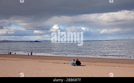 Portobello, Edimburgo, Scozia, Regno Unito. 30 Marzo 2020. Tempo, pomeriggio nuvoloso in spiaggia molto tranquilla con doccia a pioggia occasionale. Veryfeww persone seduti e a piedi sulla spiaggia di sabbia. Foto Stock