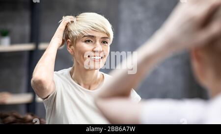 Donna con capelli corti toccare capelli in piedi in bagno, Panorama Foto Stock