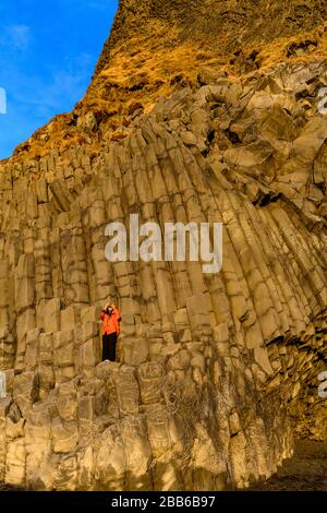 Donna in piedi sulle colonne di basalto a Reynisfjara scattare una foto, Islanda del sud, Islanda Foto Stock