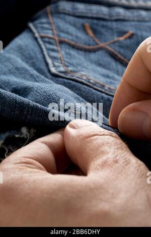 Cuciture a mano maschile tessuto strappato su jeans denim blu - moda mending o riparazione concetto, selettiva messa a fuoco Foto Stock
