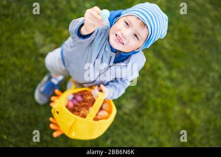 Ragazzino che indossa maschera protettiva alla caccia dell'uovo di Pasqua nel giardino primaverile. Foto Stock