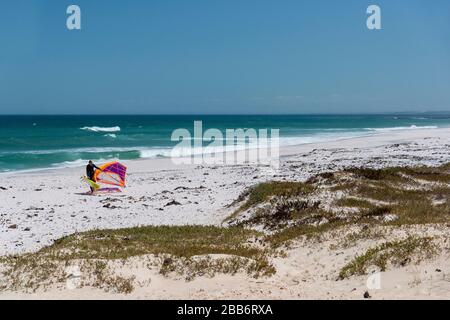 Windsurfer trasporta il carro lungo il famoso, ventoso, kite surf spiaggia a Haakgat Point, otto due Plessis Drive, Melkbosstrand, città di Capte, Sud Africa Foto Stock