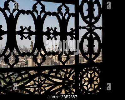 uno sguardo attraverso una splendida finestra decorata tipica di una moschea sullo skyline della città del cairo con le sue moschee e minareti Foto Stock