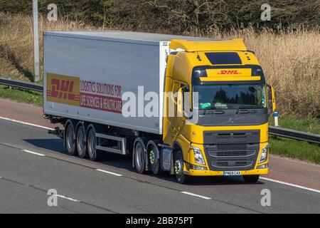 Spedizione internazionale DHL; autocarri gialli per la consegna in trasporto, camion, trasporto, camion Volvo FH, cargo carrier, veicolo, trasporto commerciale, industria, M6 a Manchester, Regno Unito Foto Stock